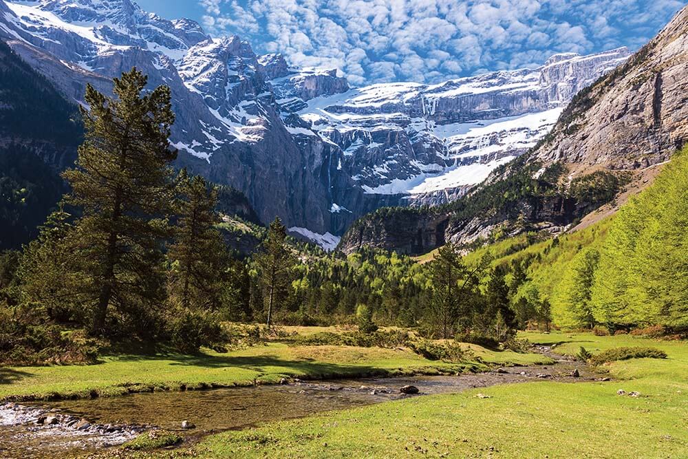 Snow-streaked cirque above a green meadow and mountain stream