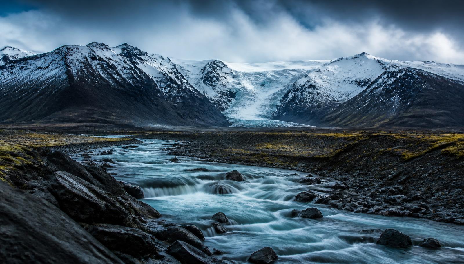 Glacial river running through black volcanic rock beneath Icelandic mountains