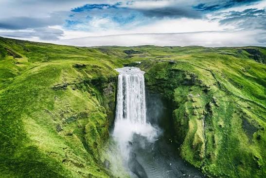 Skógafoss waterfall falling between bright green Icelandic hillsides