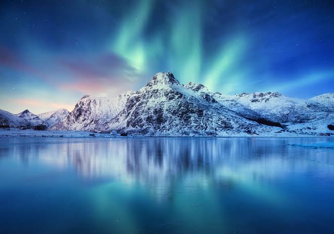 Northern lights over snow-covered peaks reflected in a Lofoten fjord