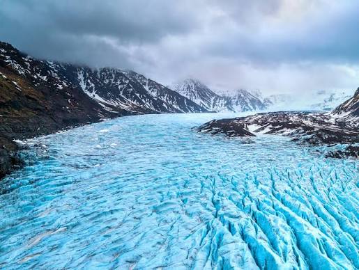 Blue glacier tongue crevassed between snow-covered Icelandic mountains